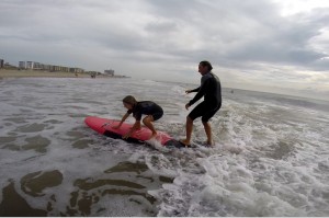 Instructor helping girl stand up on surfboard