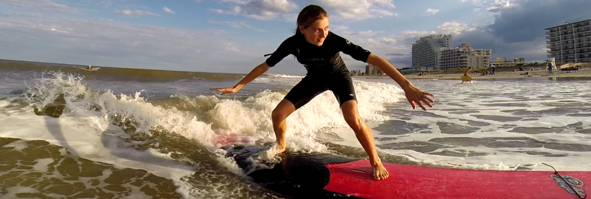girl balances on red surfboard in black wetsuit